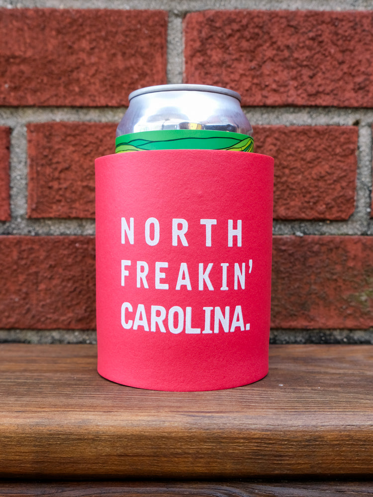 A red foam koozie featuring the bold text 'North Freakin' Carolina' printed on the front in white font. The koozie is designed to keep your beverage cool and fits most standard cans or bottles.