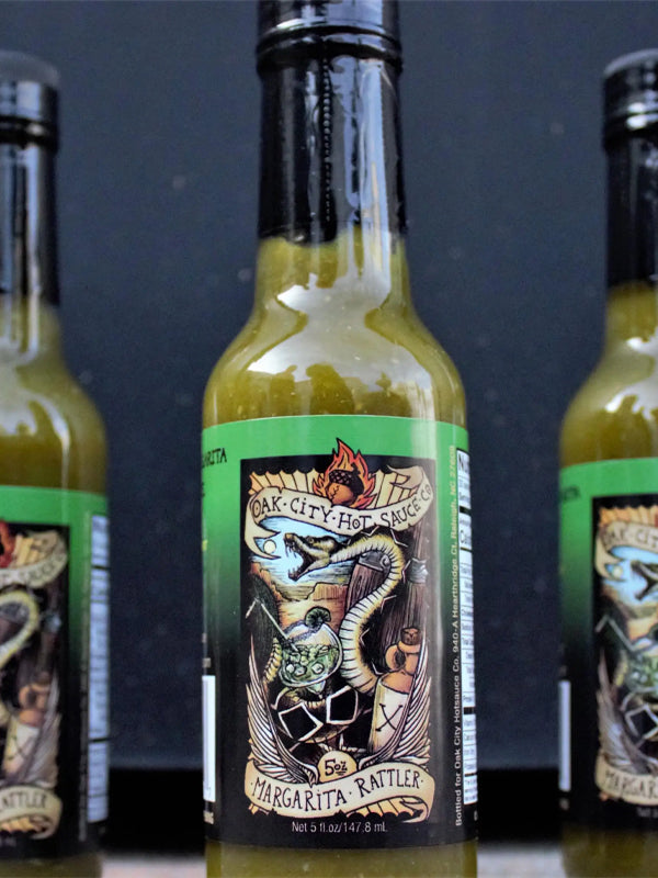 A 5 oz. bottle of Margarita Rattler Hot Sauce, combining zesty lime, tequila, and a spicy kick, perfect for adding a bold, tangy flavor to your tacos, grilled meats, or cocktails.